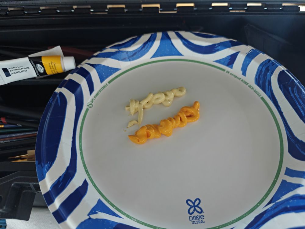 Two shades of yellow acrylic paint on a paper plate. 