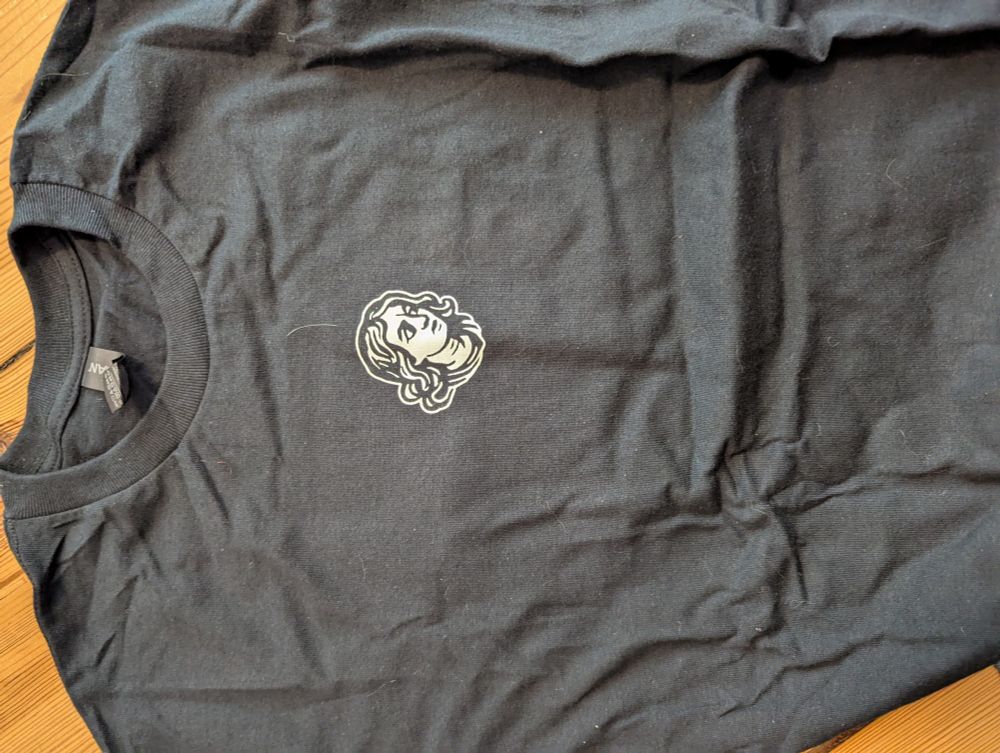 Vorderseite eines T-Shirt in schwarz. Zu sehen ist ein Kopf 