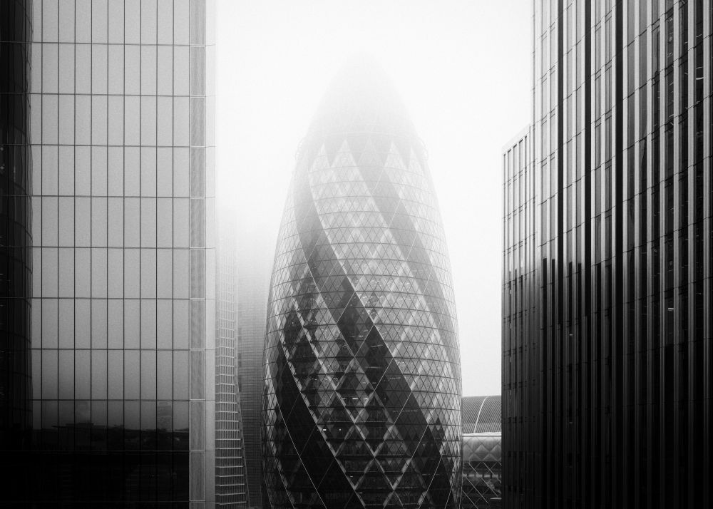 This is a black and white image of a foggy London scene. The image shows buildings to the left and the right, with the Gherkin building in the centre. There is heavy fog at the top of the scene, masking the top of the Gherkin.