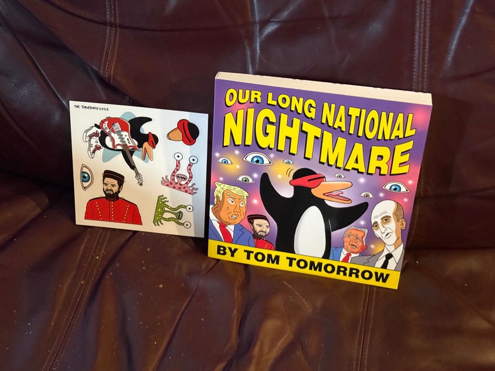 The new book Our Long National Nightmare by Tom Tomorrow and enclosed sticker sheet, propped on the couch.