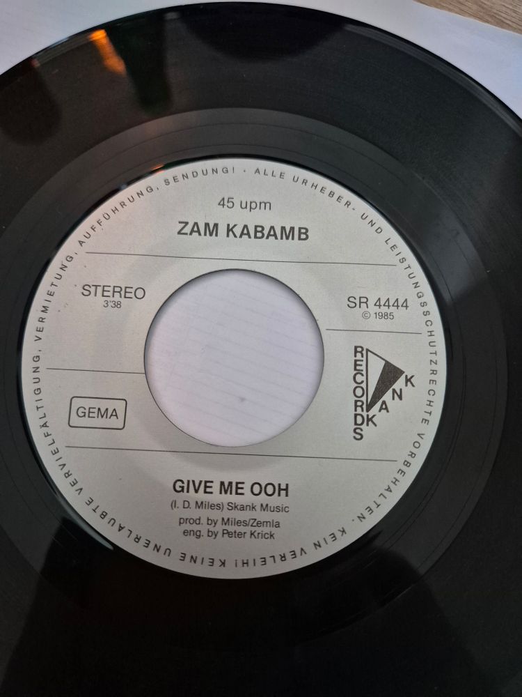 A 7-inch vinyl record showing the song title Give Me Ooh and artist Zam Kabamb released on Skank Records in 1985.