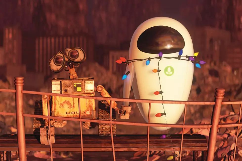 A still from the movie WALL-E featuring two robotic characters, WALL-E, small and boxy with expressive binocular-like eyes, and EVE, sleek and egg-shaped, standing on a bridge. WALL-E is adorned with Christmas lights that also wrap around EVE, creating a warm and festive atmosphere. The background depicts a dystopian, rubble-filled landscape bathed in warm hues.