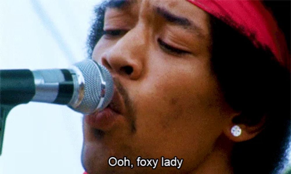 a close up of a man singing into a microphone with the words ooh foxy lady above him