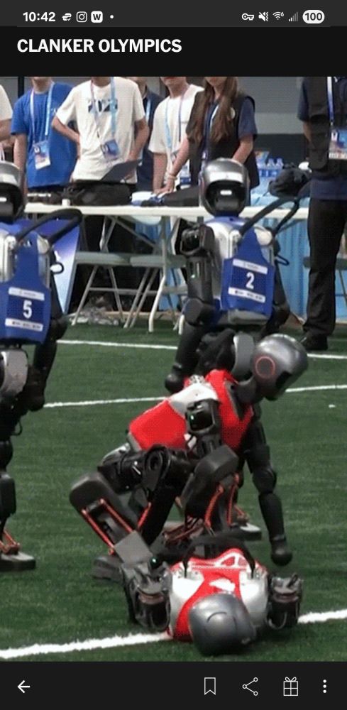 An image depicting two humanoid robots in red jerseys, two in blue jerseys, and an audience of humans in the background. The robots are on a sports field of some kind. One Red-jersey robot is on the ground with the other crouched down in front of it. The image caption reads "Clanker Olympics"