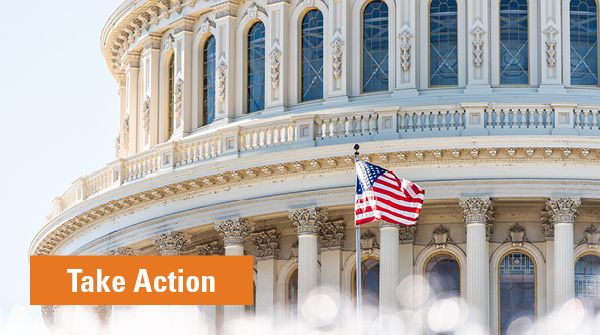 Close-up of the U.S. Capitol dome with an American flag waving in front under clear skies.