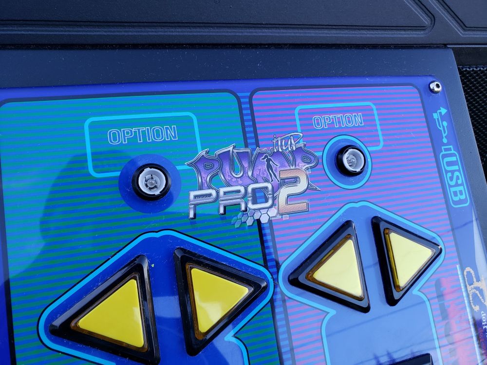 A close-up photo of the button panel, sporting the Pro 2 logo. The "OPTION" buttons normally have red caps on them, which have since gone missing. This photo was taken outdoors after moving the cabinet out of the U-Haul truck, and a reflection of the sky can be seen in the acrylic.