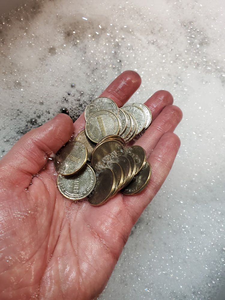 A few tokens in my hand, above soapy water. They are noticeably shinier than they were previously
