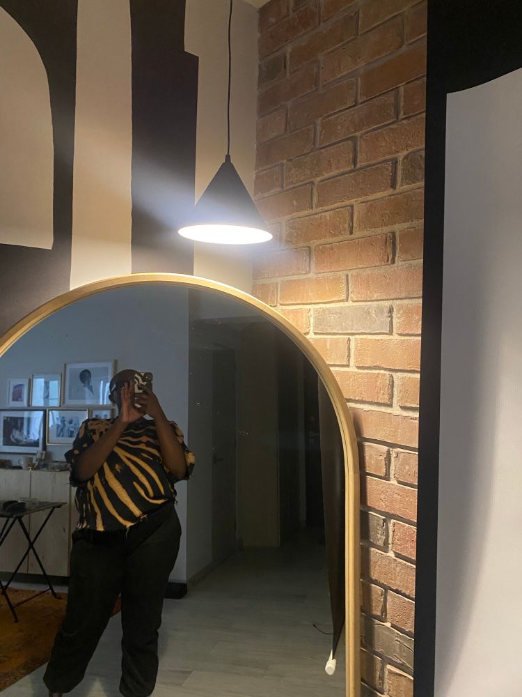 @terrysburner taking a picture of her new lamp in a mirror with a black and white striped wall behind it and an exposed brick wall.