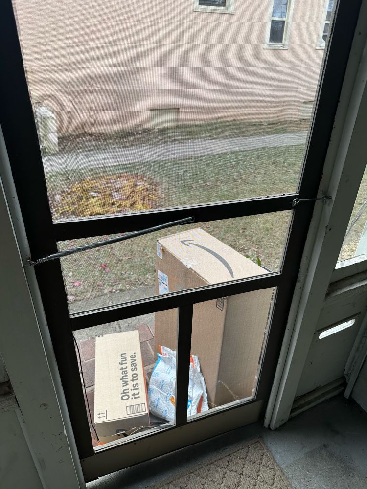 Photo of Amazon packages seen through a screen door. The packages are blocking the door from being opened. 