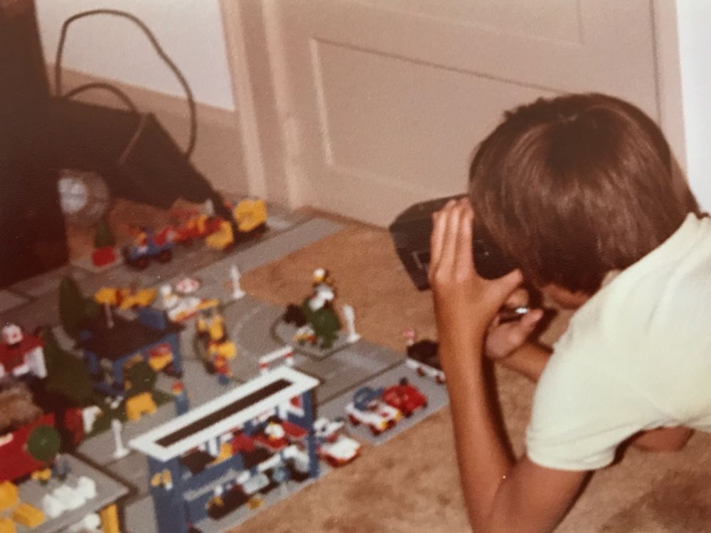 Me as a teen filming a Lego stop motion movie. There is are several Lego City sets on the floor. 