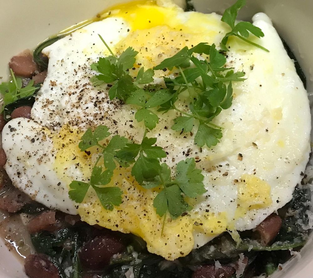 A bowl of beans and greens topped with an egg and parsley