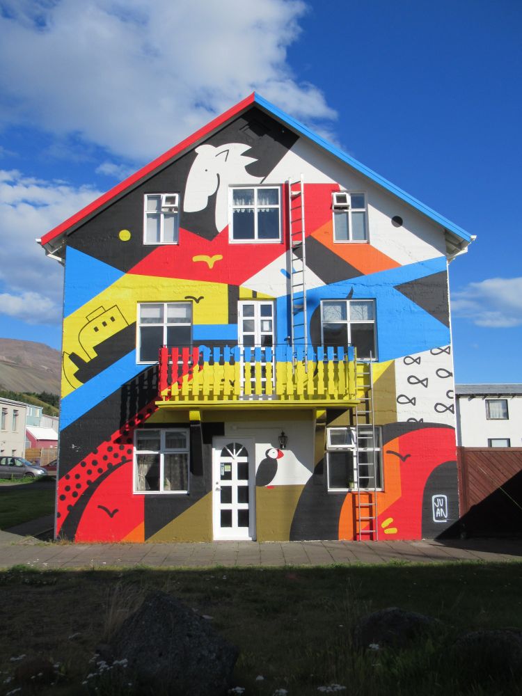 Façade du petit hôtel 550 Guesthouse. La façade présente une murale aux couleurs vives présentant des motifs de la vie en Islande (bateau, macareux, cheval, poissons). Sauðárkrókur (août 2025).