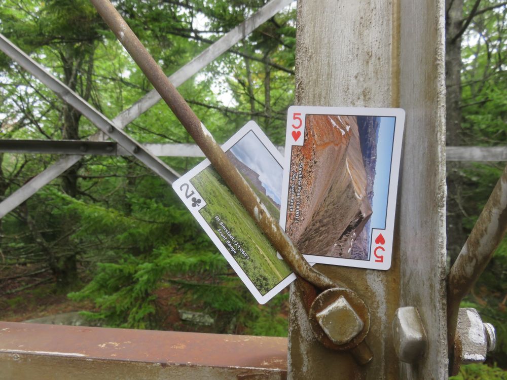 Carte numéro 2 et 5 d'un jeu de cartes illustrées par des montagnes du Colorado. Les cartes sont sur une tour de guet. On ne voit qu'une partie de la tour. Il y a des arbres en arrière-plan. 