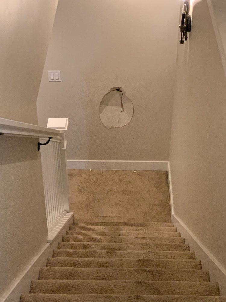 A picture of stairs with a suspiciously human head shaped hole in the wall at the bottom
