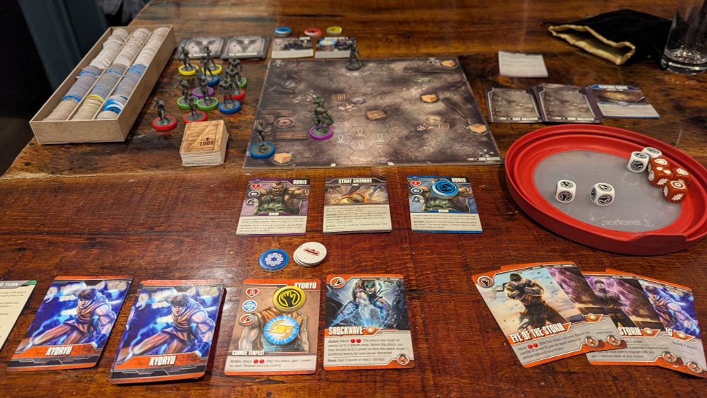 A photo of the boardgame Street Masters, featuring a hex grid board that represents a fighting arena, with some video game style fighter miniatures on it. Around the board are various cards, dice, tokens, and more miniatures. 