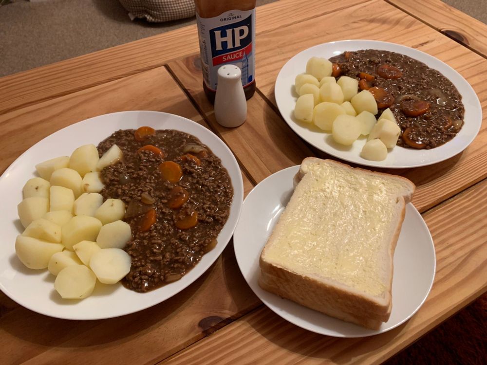A photo from the classic "best homemade dinner on the planet" featuring two plates of mince meat with carrots and onions mixed in, boiled potatoes, buttered white bread and a bottle of HP sauce. Charitably I would not call it the best homemade dinner on the planet, but if it makes you happy, original photographer, good for you.
