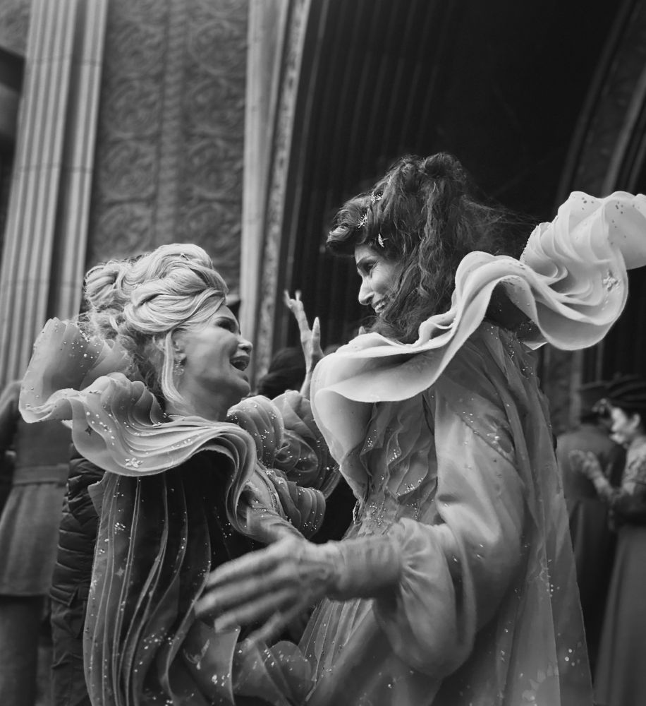 Black and white photo of Idina Menzel and Kristin Chenoweth in costume on the set of the Wicked film.