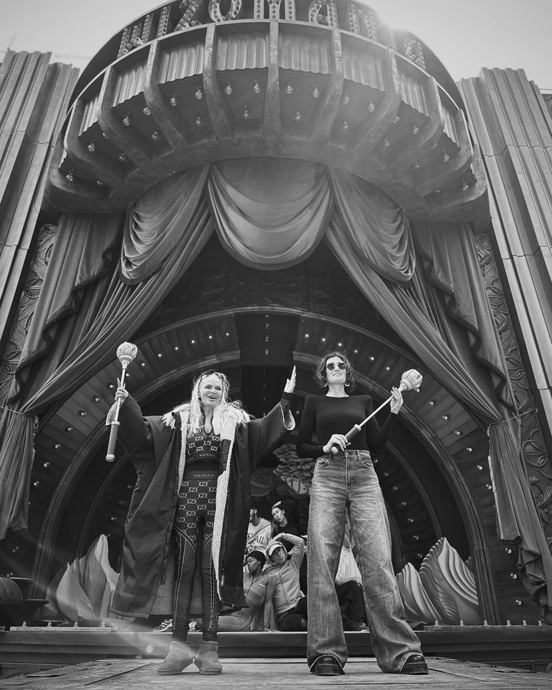 Black and white photo of Idina Menzel and Kristin Chenoweth dressed casually rehearsing on the set of the Wicked film.