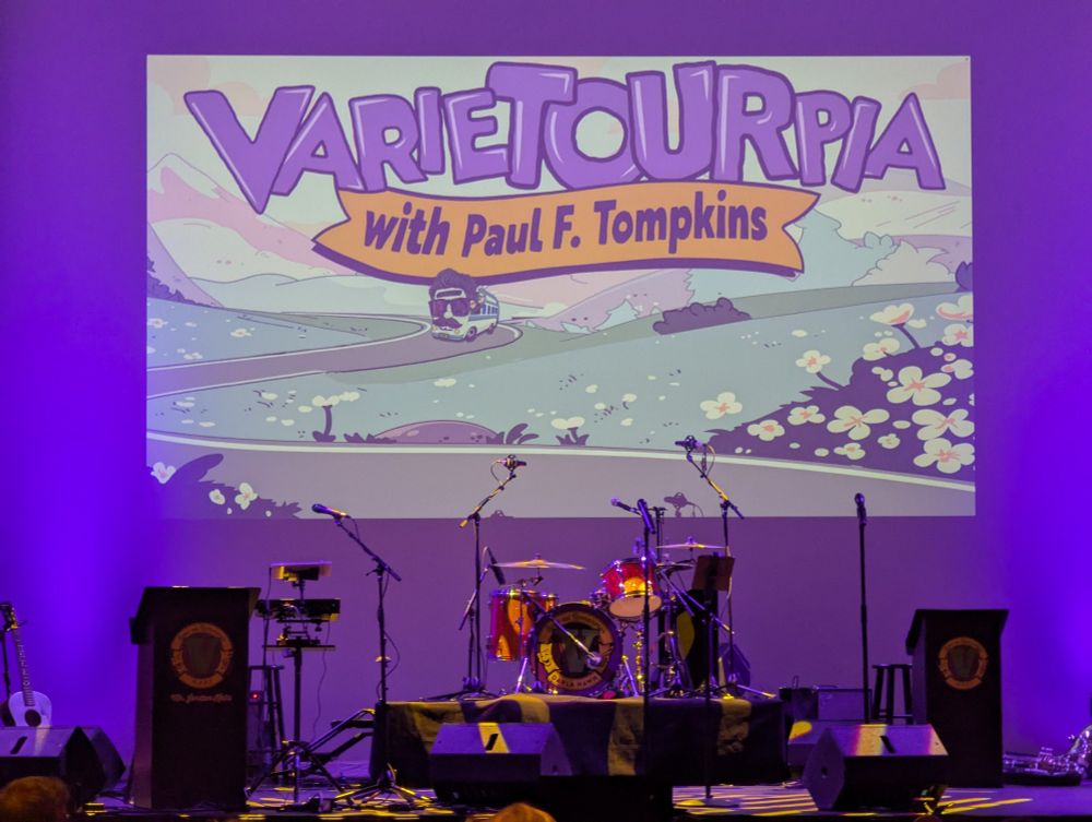 Stage before the show with projected banner that says Varietourpia with Paul F Tompkins.