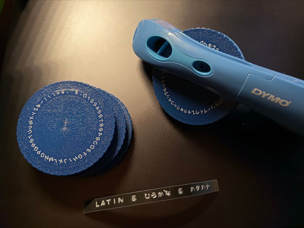 Light blue manual embossing label maker on a dark background with three alternate wheels next it.