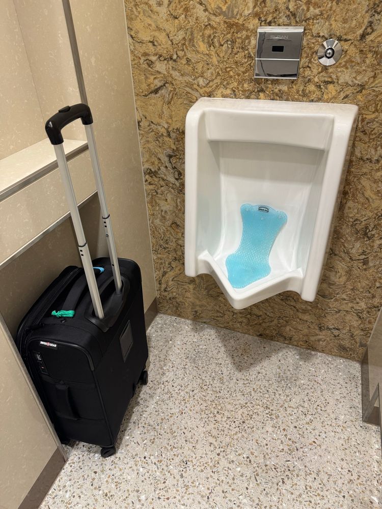 A urinal at Minneapolis airport with enough lateral space for suitcase AND human, side by side, thanks to a recessed space in the divider.