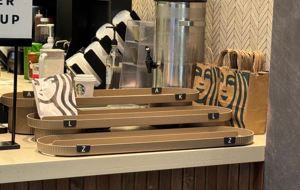 Three ready-for-pick-up trays in an airport Starbucks with baffling labels…