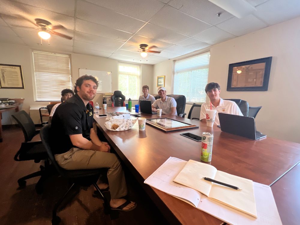 The Executive Board of the Gamma Iota Chapter of the Sigma Nu fraternity at the University of Kentucky in Lexington, seated and smiling around the board table on  a Sunday advisor update. VP, Recruitment, Housing, Recorder and Treasurer. 