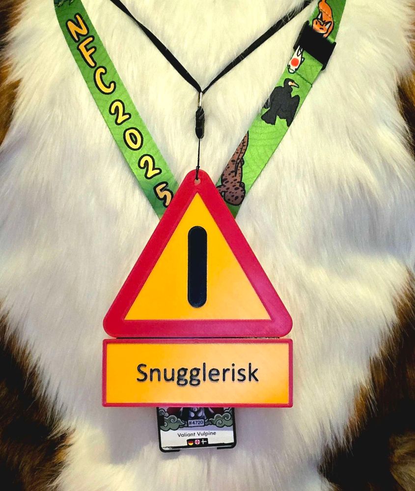 3D-printed fursuit tag in the shape of a warning sign saying "Snugglerisk", worn along with the NFC 2025 fursuit badge by a person in a fox fursuit.