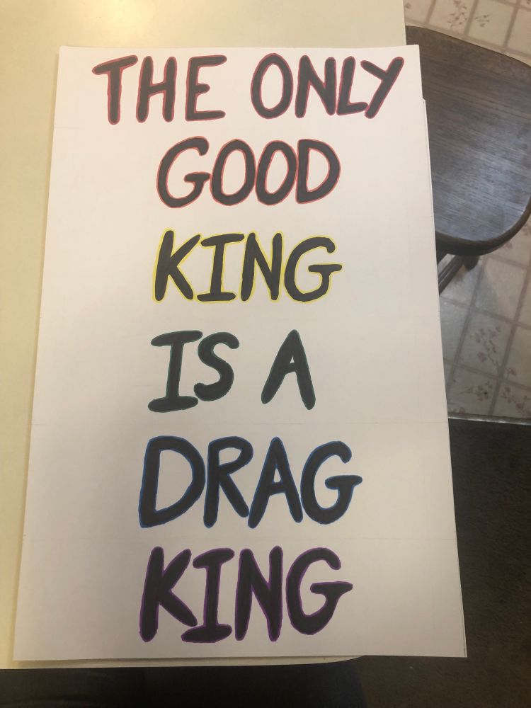 Protest sign saying “the only good king is a drag king” in bold black-sharpie capitals with rainbow outlines.