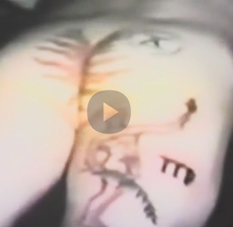 Screen Capture of video segment featuring a tattooed male butt; flames come out of the crack and there's a male nude on the thigh
