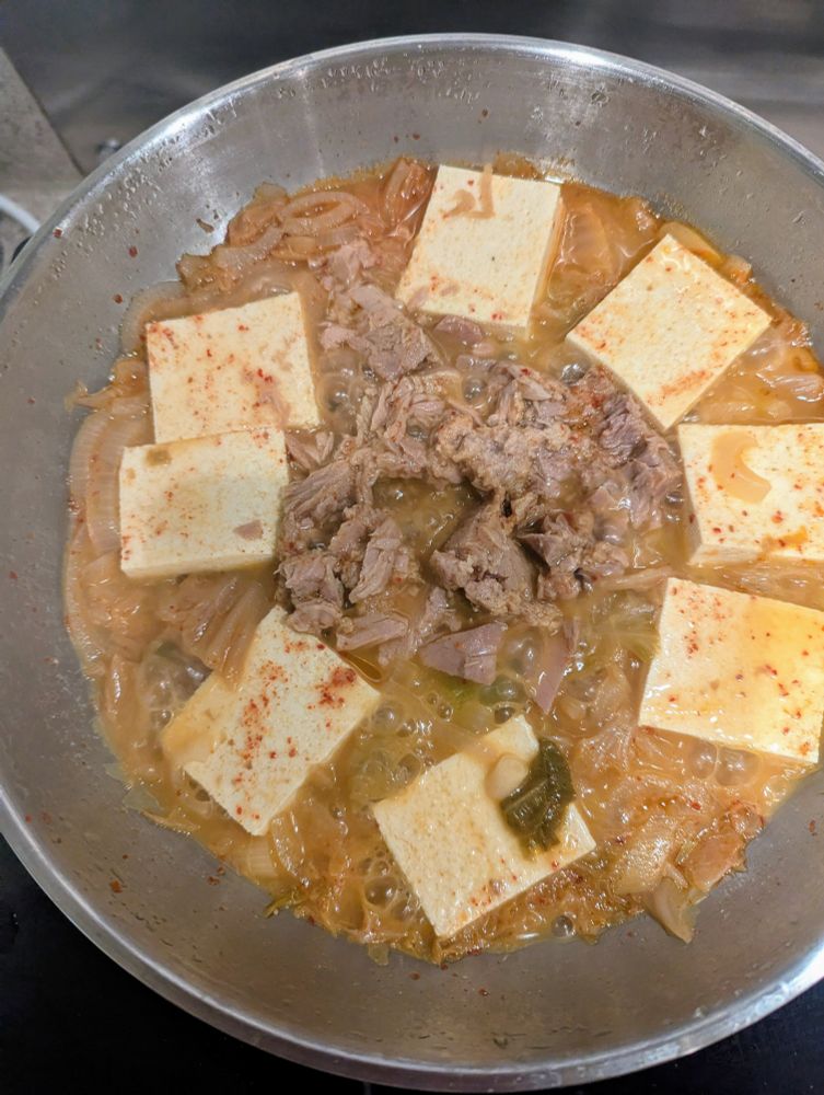 Kimchi stew in a silver frying pan with tuna and tofu arranged on top