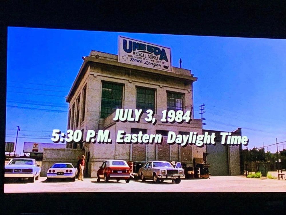 A frame from the beginning of The Return of the Living Dead. We see the Uneeda Medical Supply warehouse exterior. A title says "JULY 3, 1984 / 5:30 P.M. Eastern Daylight Time"