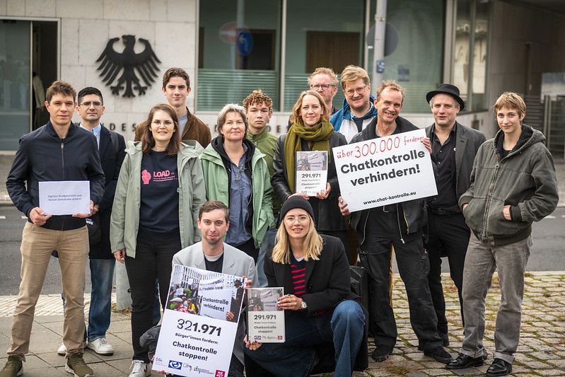 Foto: 20 Menschen stehen in einer Gruppe vor dem Eingang des Innenministeriums Berlin. Die Demonstrierenden halten mehrere Plakate, darunter eines mit der Aufschrift 'Über 300.000 fordern: Chatkontrolle verhindern!'. Foto: Nick Jaussi / i.A.v. Campact