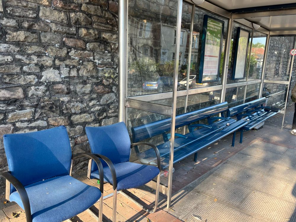 Photo of a bus stop with two additional office type chairs neatly lined up beside it 