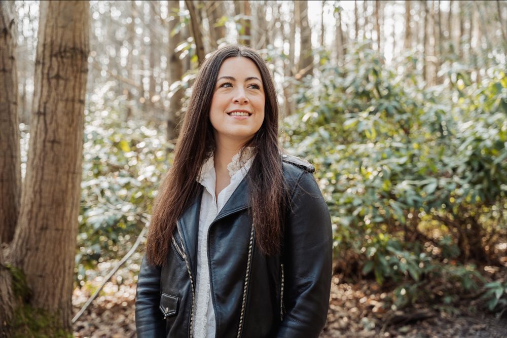 UKCF's Chief Executive, Emma de Closset, standing outside in a well-lit forest, smiling into the distance.