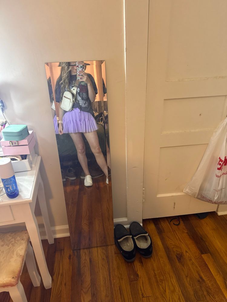 Image of the user in a mirror, wearing the gray Eras tour shirt, lilac skirt, and white tennis shoes. 