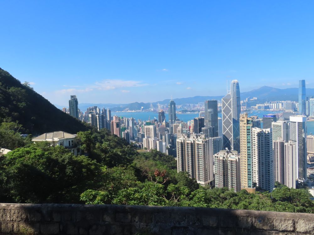 View on the road up to the Peak (aka Victoria Peak) that takes in green views, mansions on the (side of the) mountain), highrises down below, Victoria Harbour and, on the other side of it, Kowloon and the New Territories (including Tai Mo Shan, Hong Kong's highest hill/mountain -- NOT Victoria Peak).