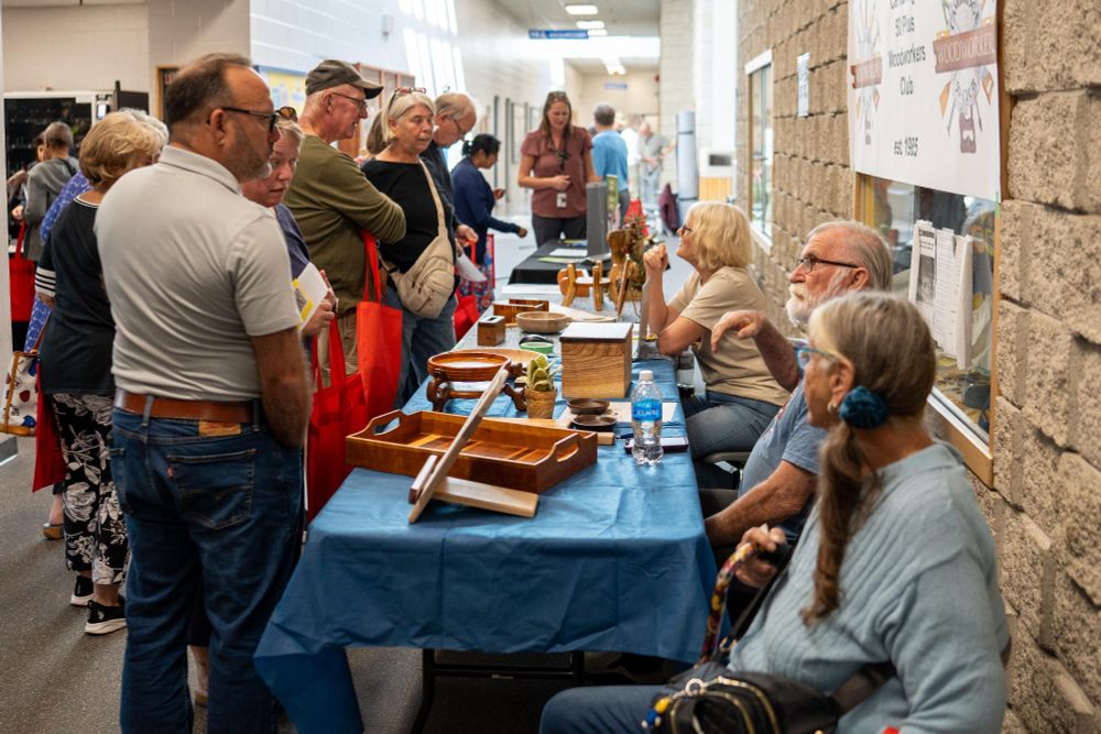 Visitors interacting with vendors at craft stalls inside a busy indoor market.