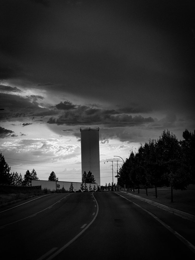 Dark clouds move in over the edge of the Prairie. A water tower is in the center of the frame.