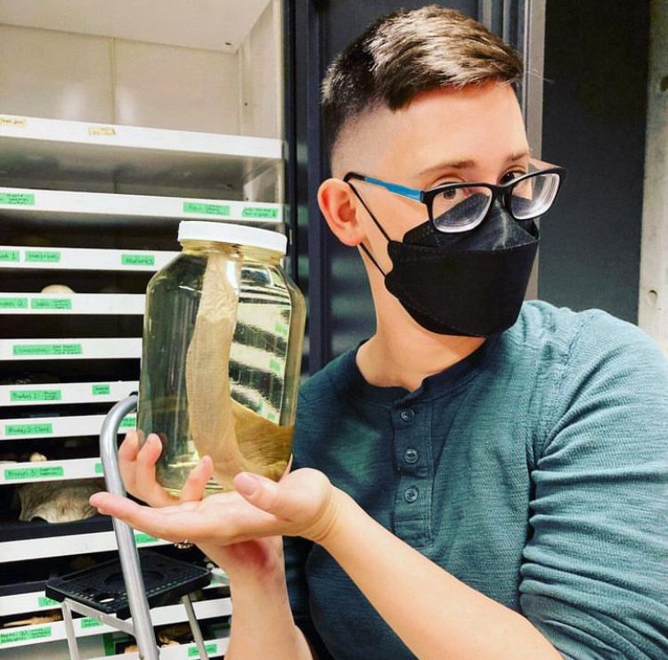 El, wearing a KF-94 mask, holds a preserved lamprey in a jar at a science museum in Vancouver.
