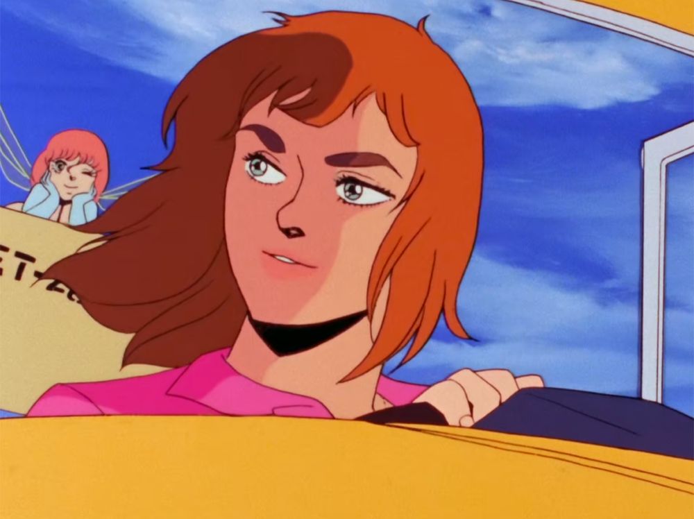 In the foreground, Marvel is smiling and looking to the side as she drives a car and her hair flows in the wind. In the background, Cham is lying down with her head in her hands, smiling, and winking.