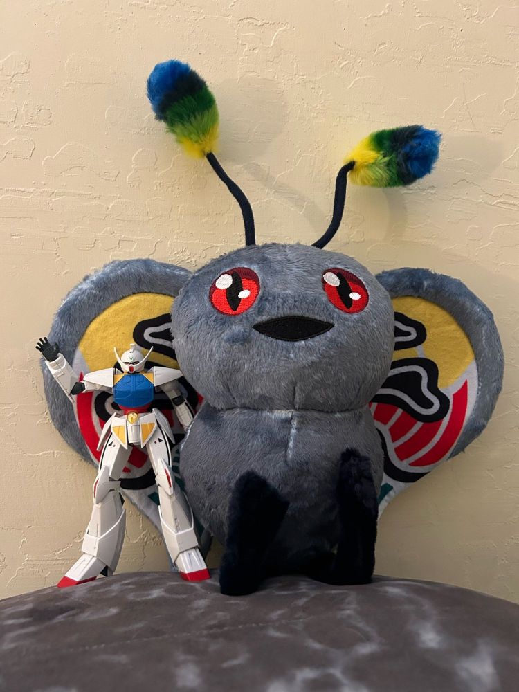 Plushie of Mothman from Megami Tensei and gunpla of Turn A Gundam standing next to each other. The Turn A is waving at you. Please wave back... 👋