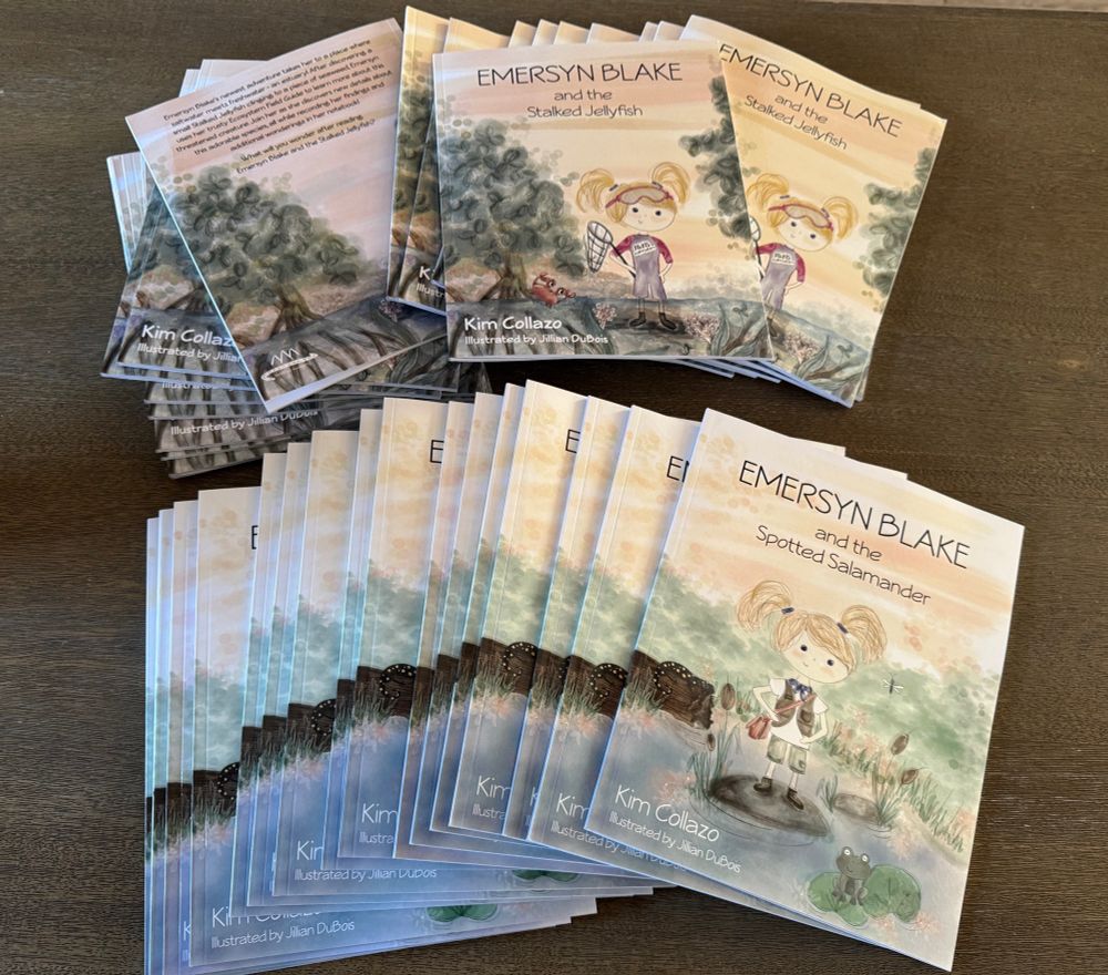 2 piles of picture books spread across a brown counter. One is copies of Emersyn Blake and the Stalked Jellyfish and the other is Emersyn Blake and the Spotted Salamander.