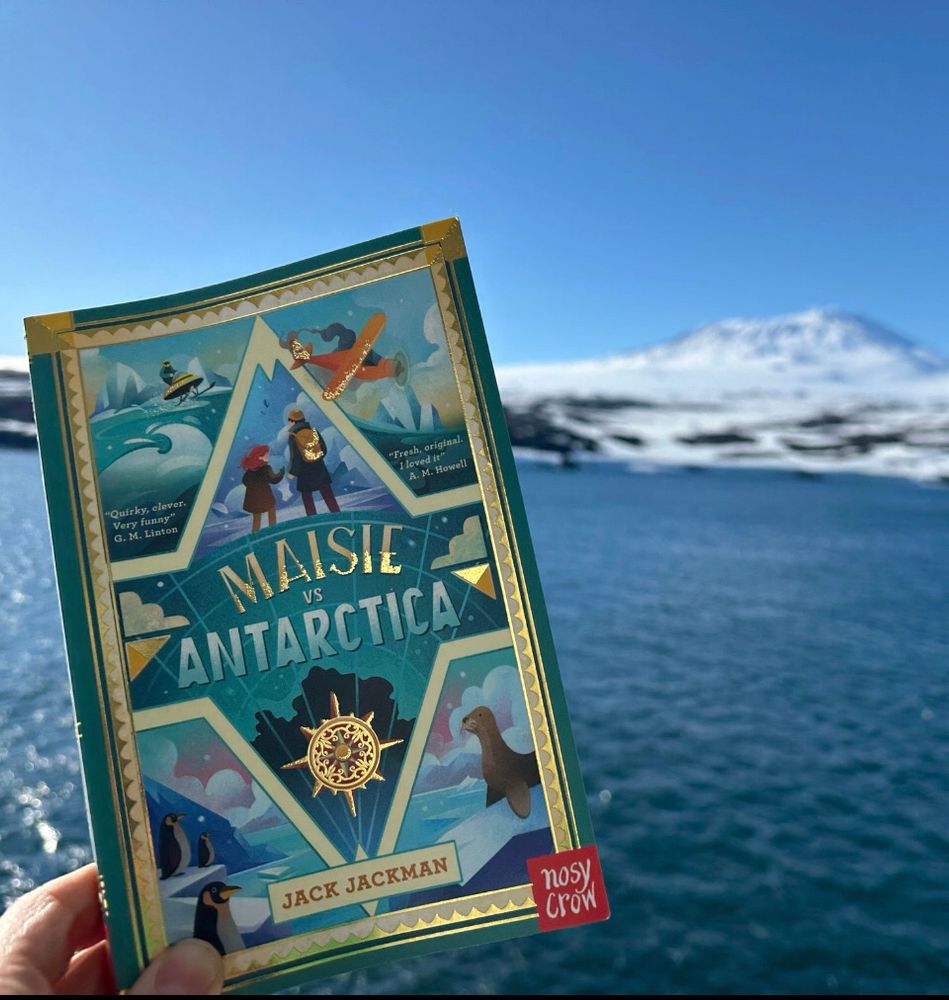 The book ‘Maisie vs Antarctica’ in front of the landscape of Antarctica.