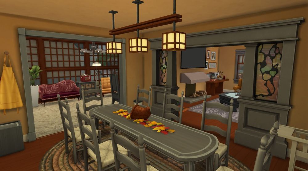 The dining room of the build. The grey archway to the living room is to the back right. To the back left is a smaller gray archway , leading to a sun room for reading. There is a large gray dining table with eight gray chairs at it. There is a centerpiece of a row of red, orange, and yellow leaves along with a cornucopia. 