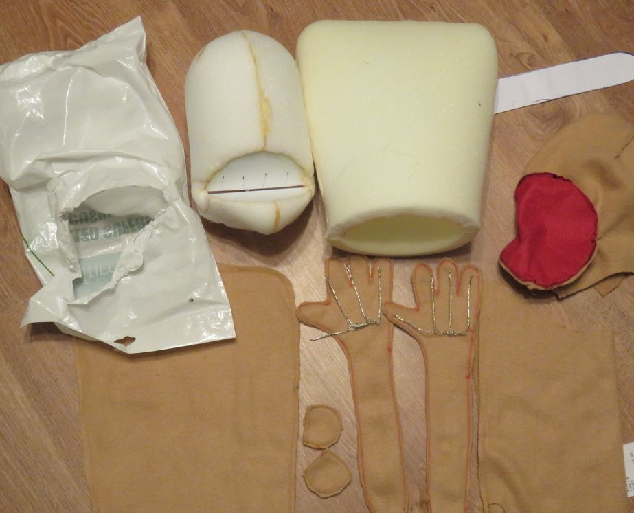 A non-constructed collection of parts for a muppet laid on the floor with a foam head and body at the top of the image and the fabric for the skin cut into arm, body, neck and head pieces at the bottom