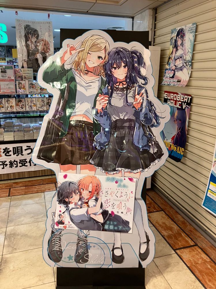 Cardboard standee of Aki and Shiho from Whisper Me a Love Song. Both girls are posing with their fingers laced and are holding up peace signs with their free hands.