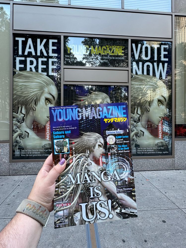 TJ’s hand holding up the special English-language edition of Young Magazine in front of Kinokuniya NY, with window displays advertising the magazine in the background.