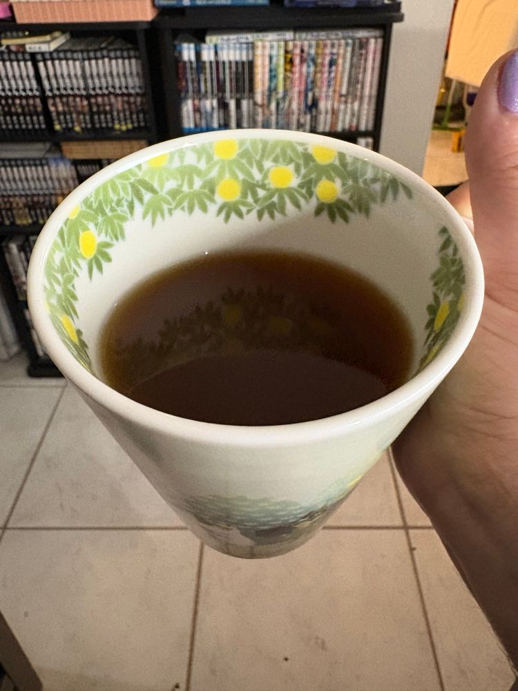 Interior of the mug, filled with black tea and featuring what appears to be lemons or round yellow fruit or flowers growing in tree branches around the inside top interior of the mug.
