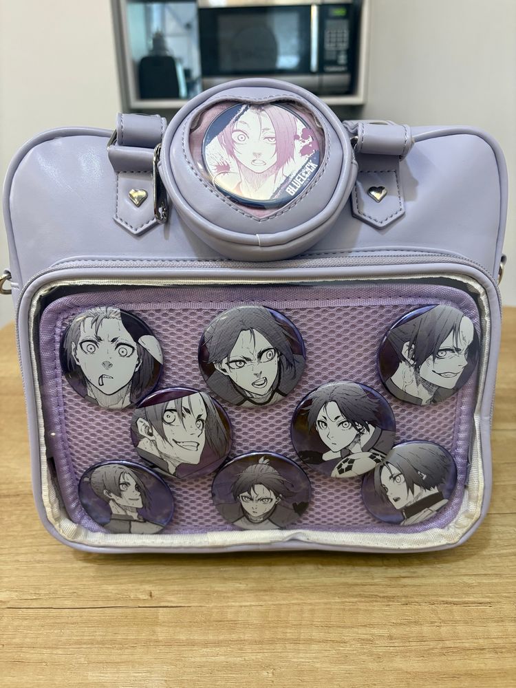 Lavender colored itabag with pins of Reo Mikage, a character from Blur Lock. The pins, a set exclusive to the Blue Lock exhibition, feature artwork of Reo from the Blue Lock manga and are a shiny metallic purple. 